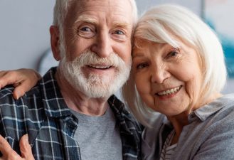 horizontal image of happy senior couple smiling and embracing while looking at camera